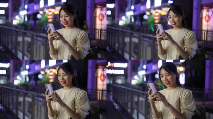 年轻的亚洲女性在夜间街头使用电话