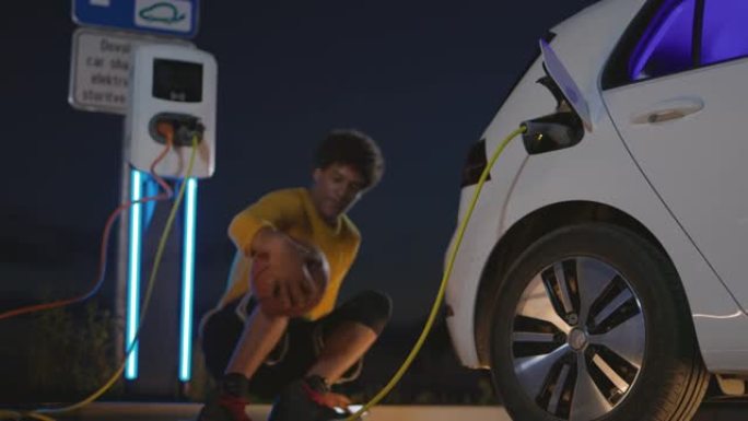 篮球运动员在将电动汽车插头插入汽车充电时使用智能手机