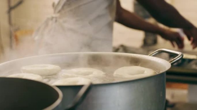 一个无法辨认的面包师在面包店的锅里炸百吉饼的4k录像