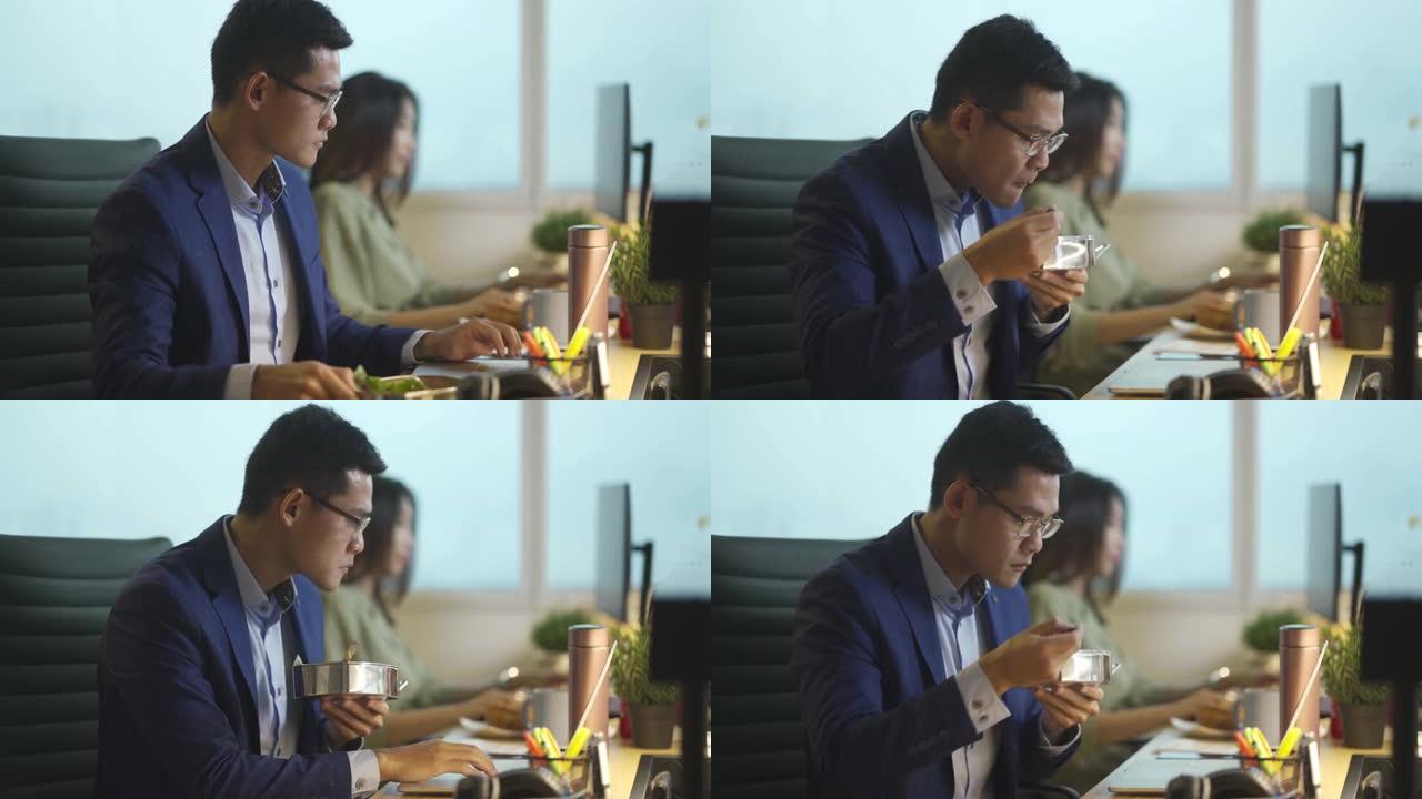亚洲华裔年轻商人在办公室工作，并在工作场所用餐nasi lemak使用笔记本电脑处理报告