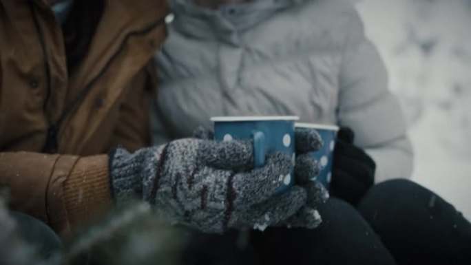 年轻夫妇在白雪覆盖的森林里喝茶牵手