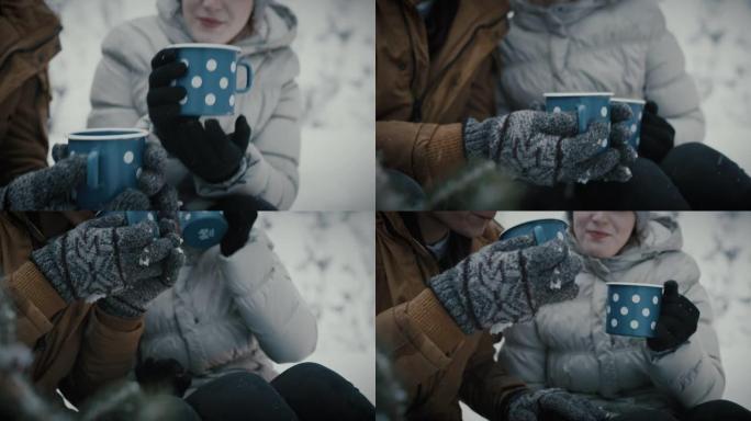 年轻夫妇在白雪覆盖的森林里喝茶牵手