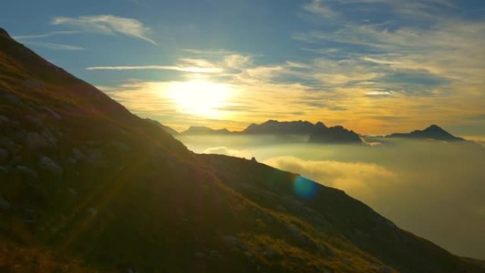 空中: 飞越金色明亮的阿尔卑斯山云层上方的空旷草地。