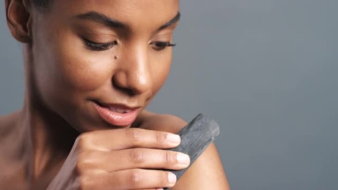 黑人妇女的皮肤，磨砂和身体护理，用木炭发光，美容和去角质。在灰色工作室模型背景下，用煤去除角质的健康