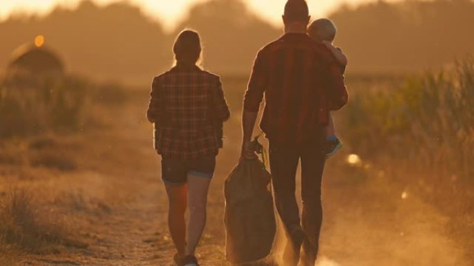 带着一个孩子的SLO MO年轻农业夫妇在日落时走在一条土路上