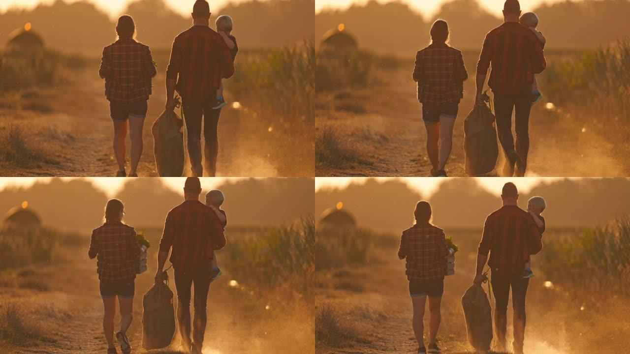 带着一个孩子的SLO MO年轻农业夫妇在日落时走在一条土路上