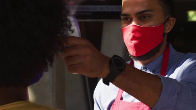 混合种族的男服务员戴着面罩为女同事测体温
