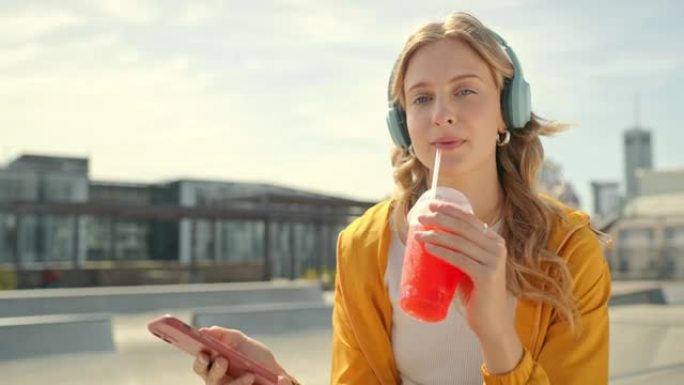 耳机、电话和z世代人在城市里喝冰沙的女人肖像。一名女性的学生、音乐和网络音频，准备在夏季旅行和度假，