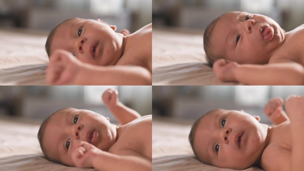 一个可爱的新生婴儿躺在床上的肖像。活跃的幼儿交流和咕咕叫。天真的大眼睛充满了惊奇，环顾四周，发现了新