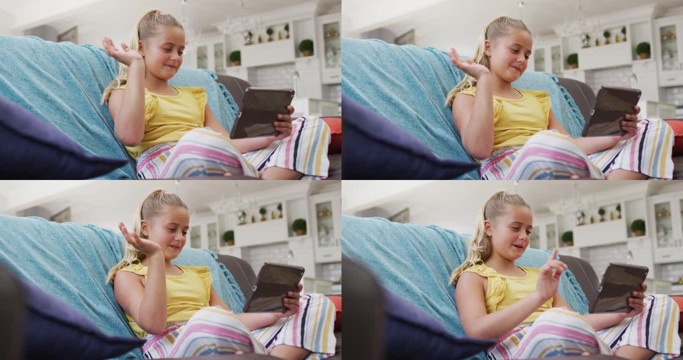 快乐的高加索女孩在家，坐在沙发上使用平板电脑进行视频通话并挥手