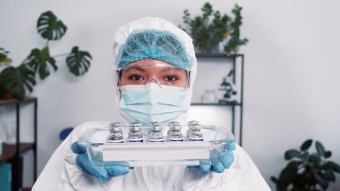 战胜冠状病毒。穿着防护服的开朗的女科学实验室工作人员展示了带有疫苗烧瓶的医疗托盘。