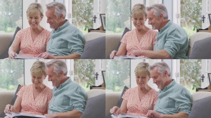 高级退休夫妇坐在家里的沙发上，喜欢看家庭相册