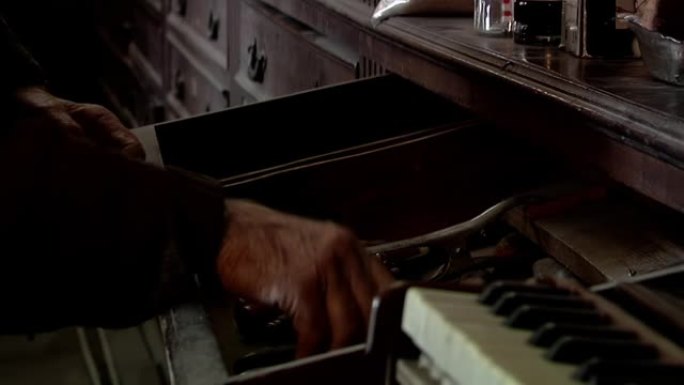 老人在他的钢琴修复车间打开一个旧橱柜的抽屉。特写。
