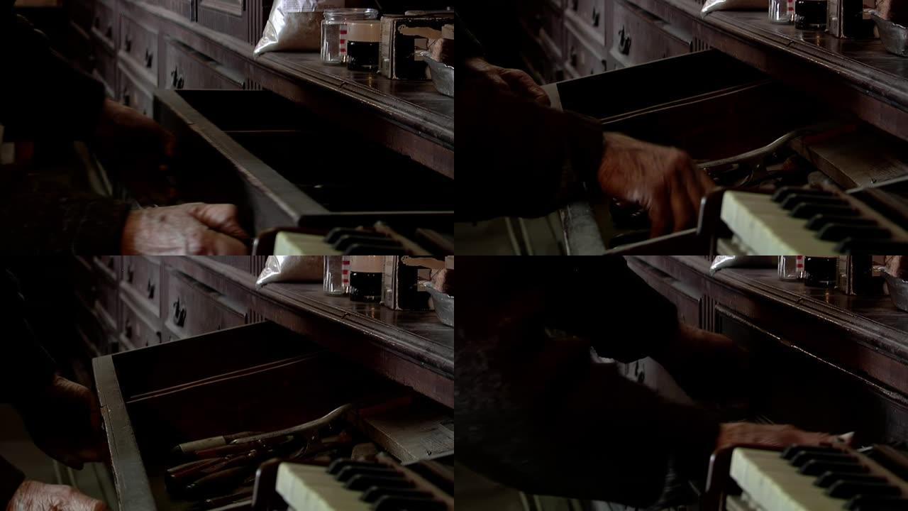 老人在他的钢琴修复车间打开一个旧橱柜的抽屉。特写。