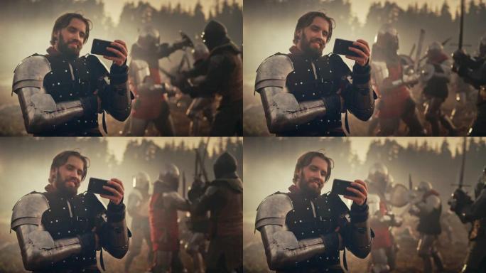 英俊的中世纪骑士在战场上微笑着用智能手机。装甲战士看在线游戏，点播搞笑视频。在背景中，战争是愤怒的