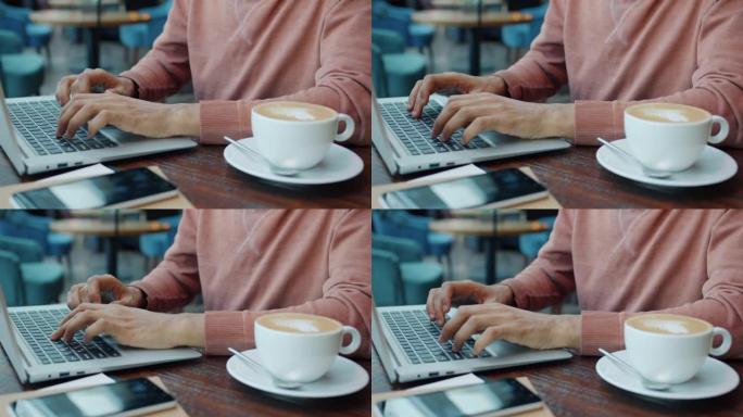 在咖啡馆里用笔记本电脑打字的男性手的特写镜头，而商人坐在桌上喝咖啡