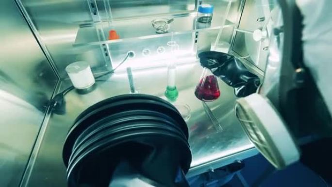 一名穿着防溅服的实验室工作人员正在真空柜中研究液体