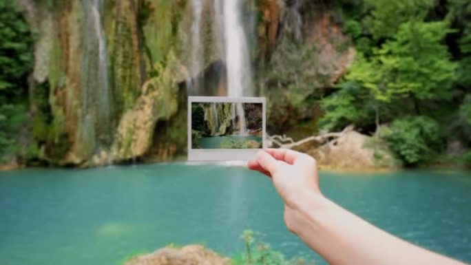 一个无法辨认的女人在瀑布前拿着宝丽来的4k录像