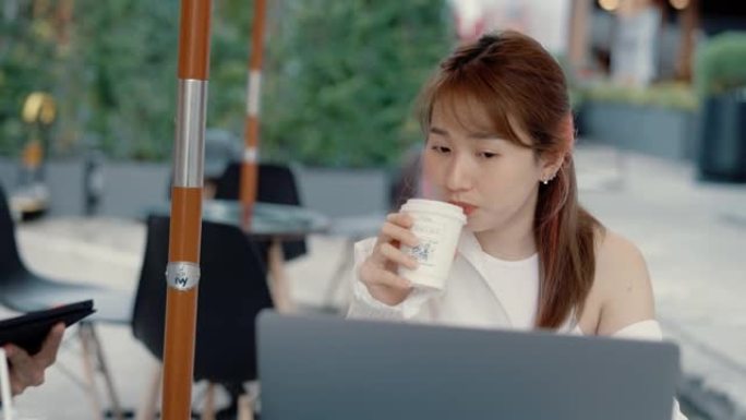 年轻的亚洲妇女在人行道咖啡馆使用平板电脑