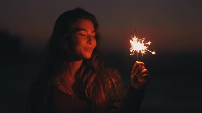 年轻漂亮的女孩晚上在海滩上拿着烟火