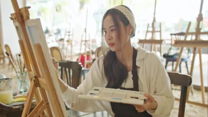 年轻的亚洲女艺术家在艺术工作室绘画日落风景画。