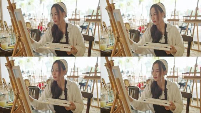 年轻的亚洲女艺术家在艺术工作室绘画日落风景画。