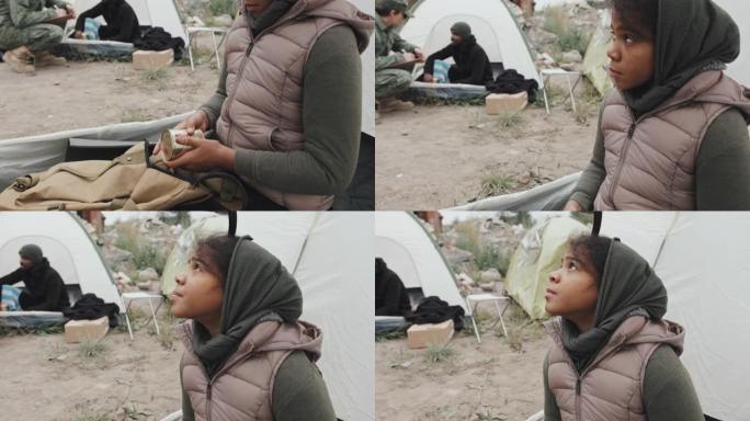 无家可归的女孩，拿着一罐食物坐在帐篷里