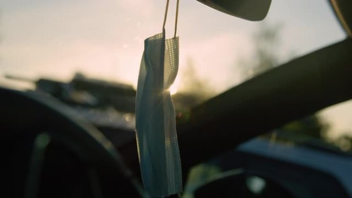 特写: 金色的早晨阳光照在悬挂在车内的医疗面罩上