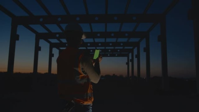 SLO MO建筑工人在黄昏时在建筑工地使用带色度键的智能手机