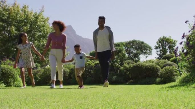 快乐的非洲裔美国父母，女儿和儿子手牵着手行走的肖像