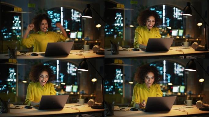 富有表现力的中东女性晚上坐在笔记本电脑上工作。项目经理收到有关她的业务提交的积极消息。兴奋的专家很高