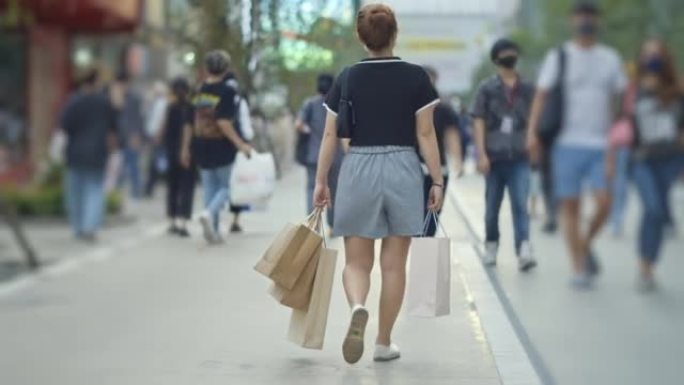 亚洲妇女在曼谷购物广场带着购物袋散步，慢动作
