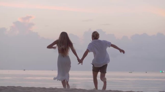 后视图，一对25-29岁的拉丁美洲和西班牙裔夫妇在奔跑和跳跃时牵手，一起享受旅行假期美丽的海滩海洋。