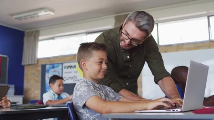 多元化的男老师使用笔记本电脑帮助坐在教室里的男生