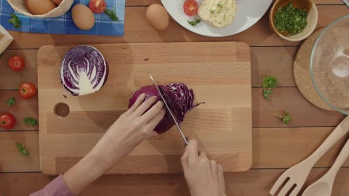 年轻的亚洲女厨师的手拿着刀在家里厨房桌子上的木板上切红卷心菜。