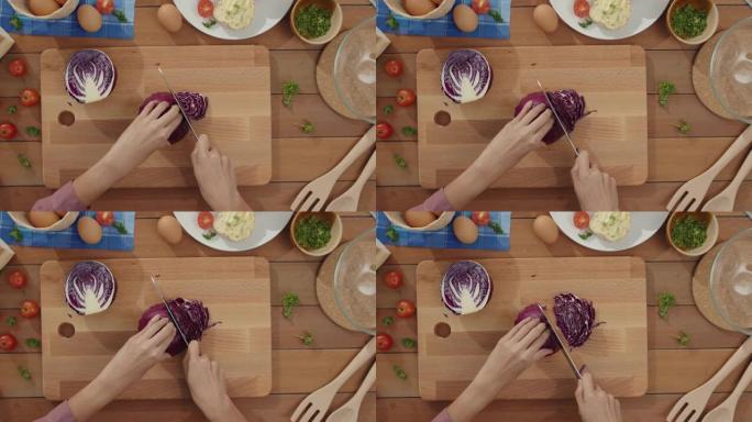 年轻的亚洲女厨师的手拿着刀在家里厨房桌子上的木板上切红卷心菜。