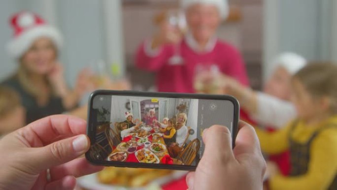 在手机上拍摄圣诞节多代家庭餐照片的POV镜头