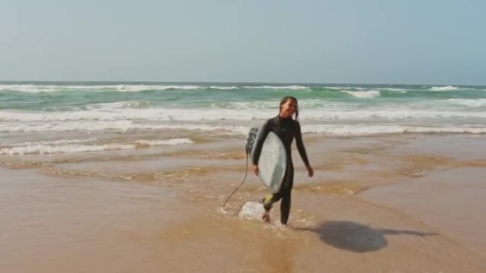 一个年轻的冲浪者在冲浪后带着冲浪板走出海洋