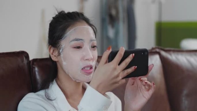 年轻快乐的女人戴化妆品面膜视频聊天