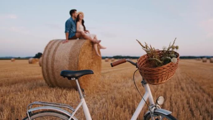 中年夫妇坐在干草捆上的手持慢动作镜头，自行车在前景中，欣赏日落