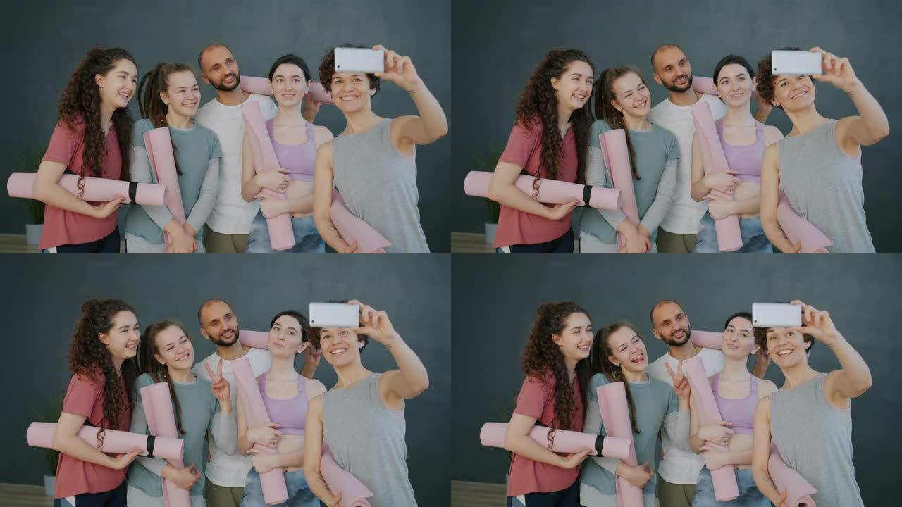 一群瑜伽学生在工作室使用智能手机相机微笑自拍照