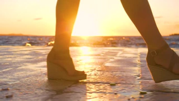 低角度: 女游客在日落时沿着田园诗般的海岸散步。