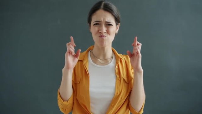 美丽的女孩在灰色背景上交叉手指祈祷手势的肖像