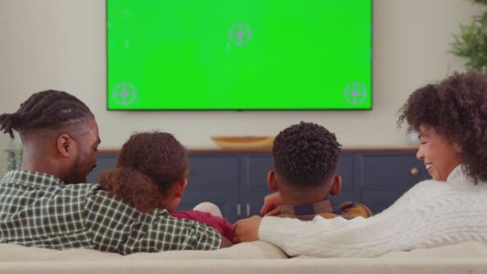 家庭坐在沙发上的后视图在家里的绿屏电视上看电影并大笑