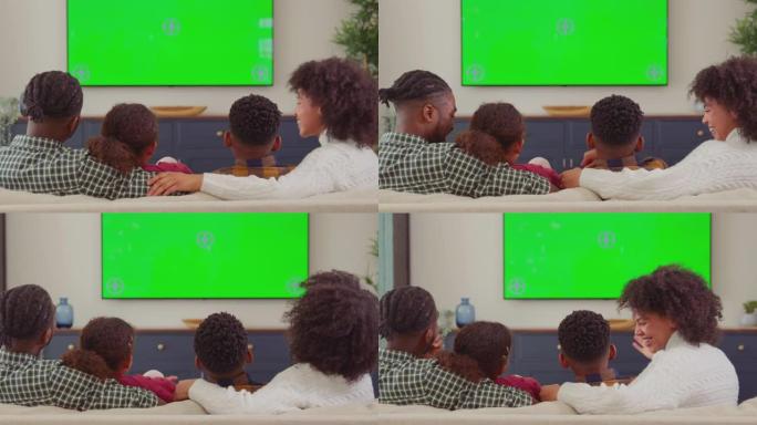 家庭坐在沙发上的后视图在家里的绿屏电视上看电影并大笑