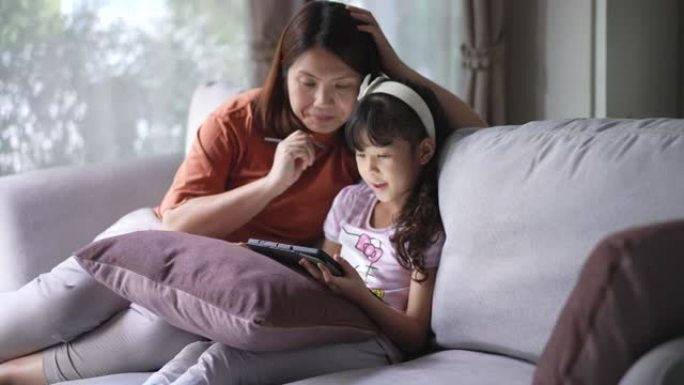 母亲在家在客厅的数字平板电脑上教女儿在线学习