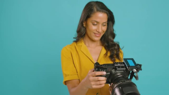 成熟的女性摄像师，在摄影棚拍摄蓝色背景下的摄像机拍摄视频