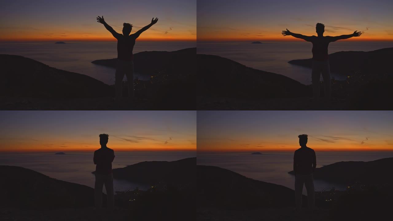 一个欣喜若狂的人在享受海上日落时向天空举起双臂的SLO MO剪影