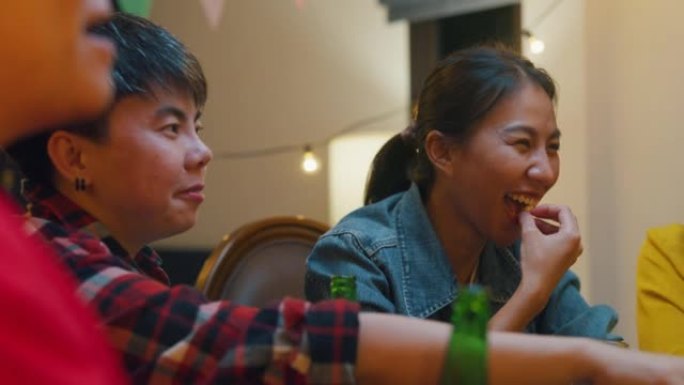一群多民族的亚洲成人朋友喝酒精啤酒瓶玻璃和有趣的谈话笑声享受夜生活室内家庭餐桌上的聚会。