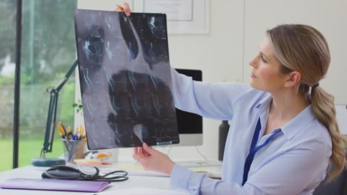 成熟的女性医生或全科医生坐在办公室的办公桌上看CT或MRI扫描-慢动作拍摄